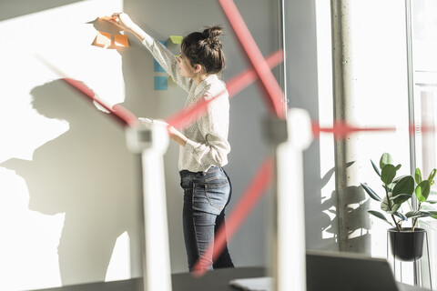 Businesswoman in office putting sticky notes on wall with wind turbine models on desk stock photo