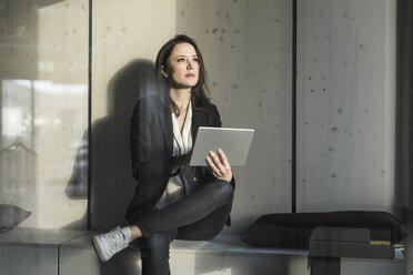 Businesswoman with tablet sitting in lounge area in office - UUF17124