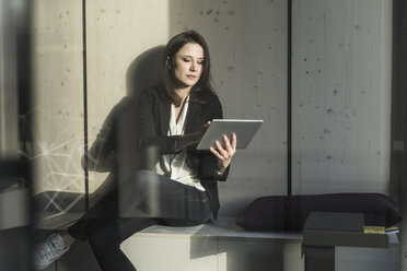 Businesswoman with tablet sitting in lounge area in office - UUF17125