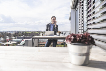 Lächelnde Geschäftsfrau mit Handy und Laptop auf der Dachterrasse - UUF17139