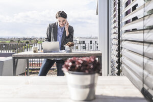 Lächelnde Geschäftsfrau mit Handy und Laptop auf der Dachterrasse - UUF17141