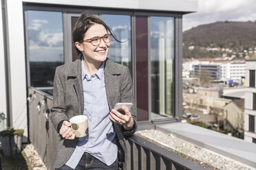 Smiling businesswoman with cell phone and cup of coffee on roof terrace - UUF17146