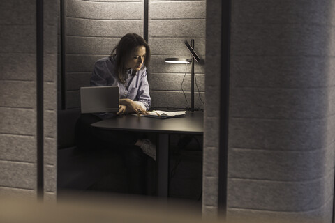 Geschäftsfrau arbeitet mit Laptop und Dokument in einer Büronische, lizenzfreies Stockfoto