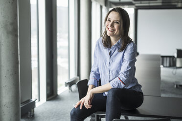 Lächelnde Geschäftsfrau sitzt am Konferenztisch im Büro - UUF17154