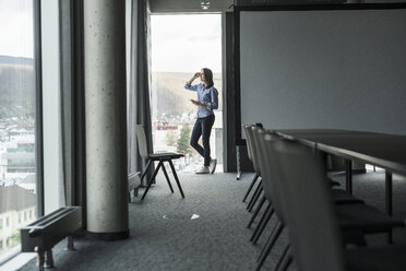 Geschäftsfrau mit Handy steht am Fenster im Büro - UUF17163