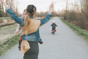 Mutter, die ihre Tochter trägt und ihren kleinen Sohn anfeuert, der Fahrrad fährt - CMSF00044