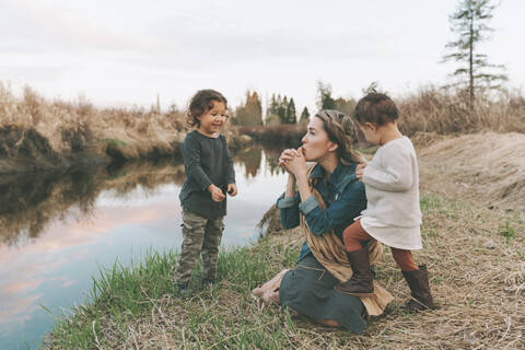 Maother and children playing with a grass blade at a river stock photo