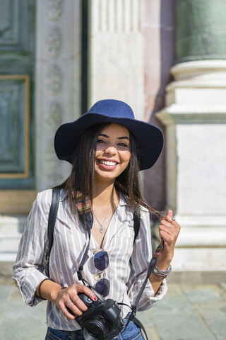 Italien, Florenz, Porträt eines glücklichen jungen Touristen mit Kamera und Sonnenbrille, lizenzfreies Stockfoto