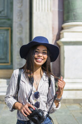 Italien, Florenz, Porträt eines glücklichen jungen Touristen mit Kamera und Sonnenbrille - MGIF00333