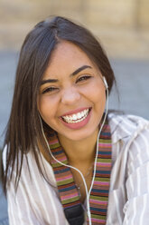 Porträt einer lachenden jungen Frau, die mit Kopfhörern Musik hört - MGIF00347