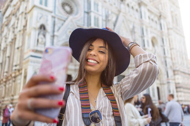 Italien, Florenz, Piazza del Duomo, Porträt eines glücklichen jungen Touristen, der ein Selfie mit seinem Smartphone macht - MGIF00350