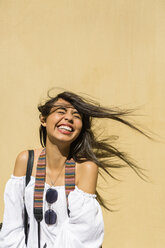 Portrait of laughing young woman with blowing hair in front of yellow background - MGIF00370
