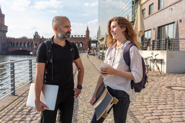 Mann im Gespräch mit Freundin mit Skateboard auf Brücke, Fluss, Oberbaumbrücke und Gebäude im Hintergrund, Berlin, Deutschland - CUF49963