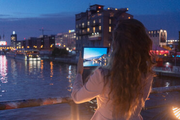 Junge Frau beim Fotografieren mit digitalem Tablet auf einer Brücke, Fluss und Stadt im Hintergrund, Berlin, Deutschland - CUF50000