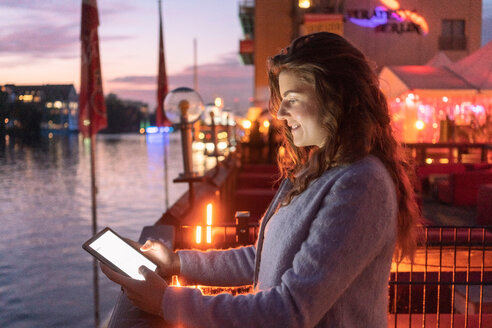 Junge Frau mit digitalem Tablet auf einer Brücke, Fluss und Stadt im Hintergrund, Berlin, Deutschland - CUF50001