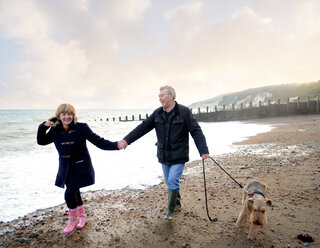 Romantisches älteres Paar hält sich an den Händen und geht mit dem Hund am Strand spazieren, Eastbourne, East Sussex, England - CUF50060