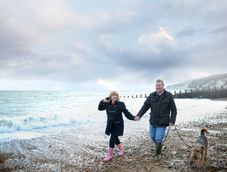 Romantisches älteres Paar hält sich an den Händen und geht mit dem Hund am Strand spazieren, Eastbourne, East Sussex, England - CUF50061