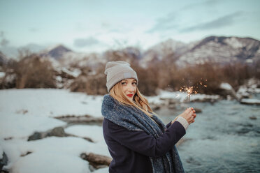 Frau mit Strickmütze und Wunderkerze am schneebedeckten Flussufer, Porträt, Orta, Piemonte, Italien - CUF50078