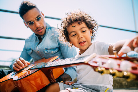 Vater bringt seinem Sohn auf der Treppe Gitarre spielen bei, lizenzfreies Stockfoto