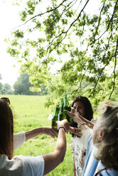 Happy women clinking beer bottles in park - IGGF00988