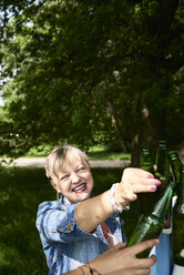 Portrait of happy woman clinking beer bottle with friends in park - IGGF00989