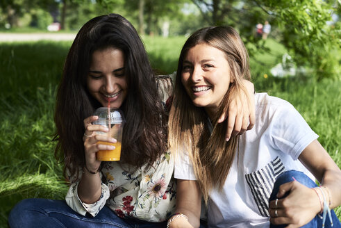 Porträt von zwei glücklichen jungen Frauen, die bei einem Picknick im Park Saft trinken - IGGF01000