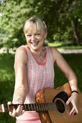 Porträt einer glücklichen älteren Frau, die im Park Gitarre spielt - IGGF01007