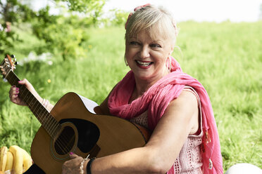 Porträt einer glücklichen älteren Frau, die im Park Gitarre spielt - IGGF01010