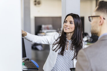 Businesswoman showing machine to businesman in a modern factory - DIGF06519