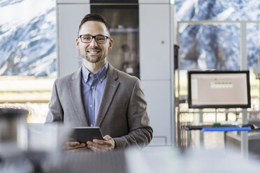 Portrait of smiling businessman with tablet in a modern factory - DIGF06525