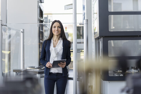 Smiling businesswoman with tablet in a modern factory - DIGF06546