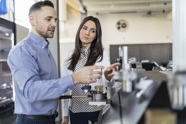 Geschäftsmann und Geschäftsfrau im Gespräch an einer Maschine in einer modernen Fabrik - DIGF06566