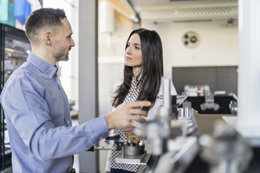 Geschäftsmann und Geschäftsfrau im Gespräch an einer Maschine in einer modernen Fabrik - DIGF06568