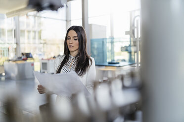 Businesswoman looking at plan in modern factory - DIGF06571