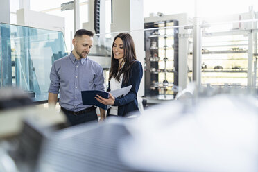 Smiling businessman and businesswoman looking at folder in modern factory - DIGF06582