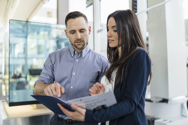 Businessman and businesswoman looking at folder in modern factory - DIGF06583