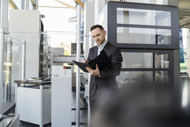 Businessman looking at folder in modern factory - DIGF06589