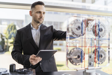 Geschäftsmann mit Tablet und Blick auf eine Maschine in einer modernen Fabrik - DIGF06603