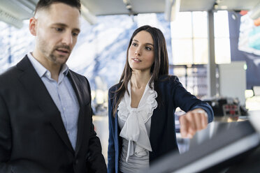 Businessman and businesswoman talking at a machine in a modern factory - DIGF06615