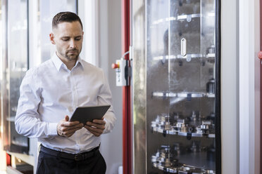 Businessman using tablet at a machine in modern factory - DIGF06633