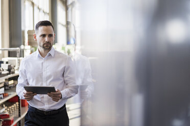 Businessman with tablet looking at machine in a modern factory - DIGF06634