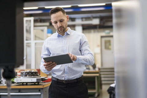 Geschäftsmann mit Tablet an einer Maschine in einer modernen Fabrik, lizenzfreies Stockfoto