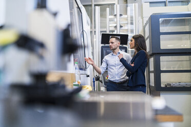 Businessman and businesswoman talking at a machine in modern factory - DIGF06663