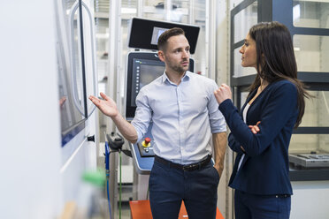 Businessman and businesswoman talking at a machine in modern factory - DIGF06664