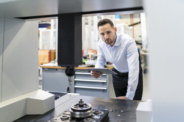 Portrait of businessman with tablet at a machine in a modern factory - DIGF06692