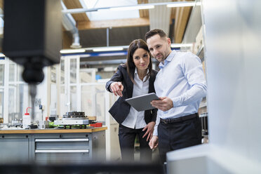 Businessman and businesswoman with tablet at a machine in modern factory - DIGF06694