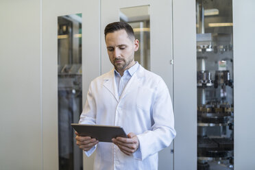 Man using tablet wearing lab coat in modern factory - DIGF06706