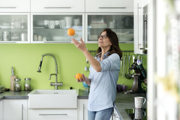 Mature woman juggling with oranges in kitchen at home - FLLF00091