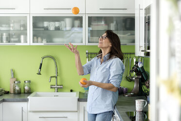 Mature woman juggling with oranges in kitchen at home - FLLF00092