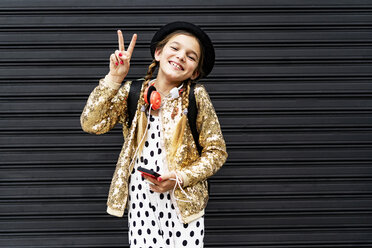 Porträt eines glücklichen Mädchens mit Smartphone, das einen Hut und eine goldene Paillettenjacke mit Siegeszeichen trägt - ERRF00894